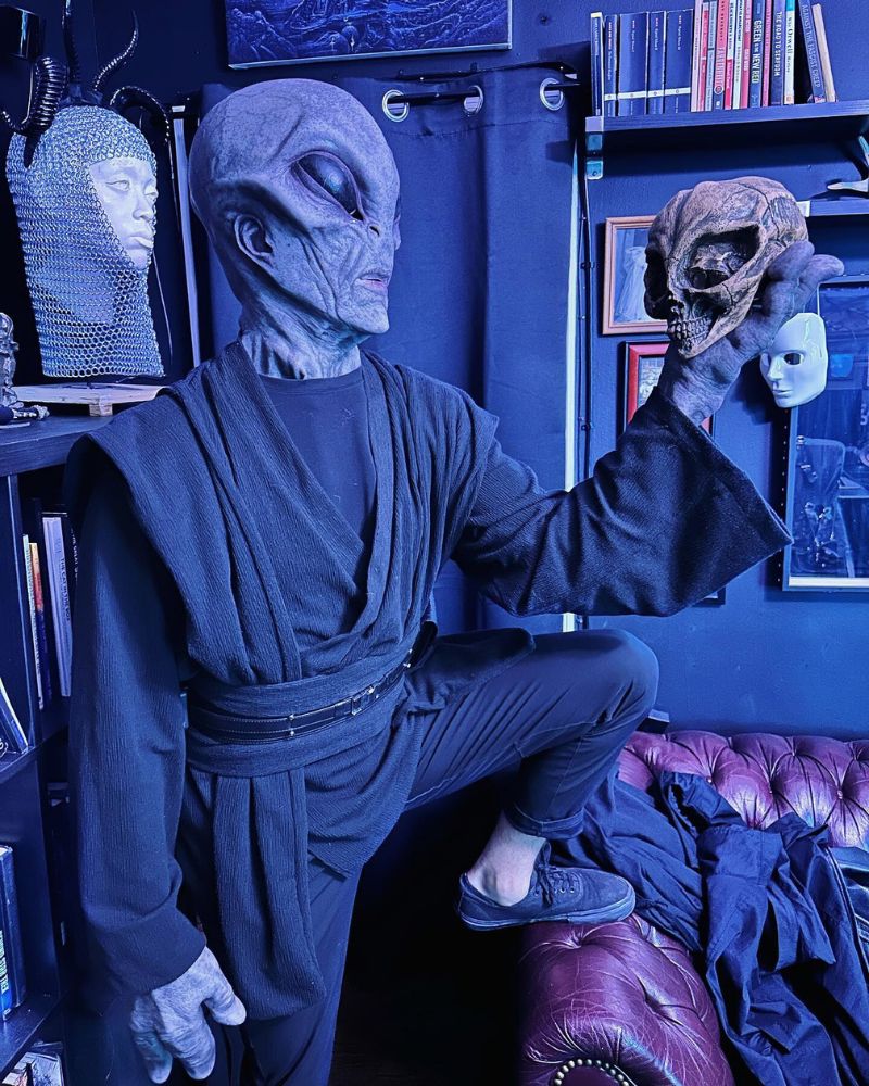 Wearing the Alien Area 51 mask and dark ceremonial robe, posing with a skull in a collector’s room — The Terror Lab.