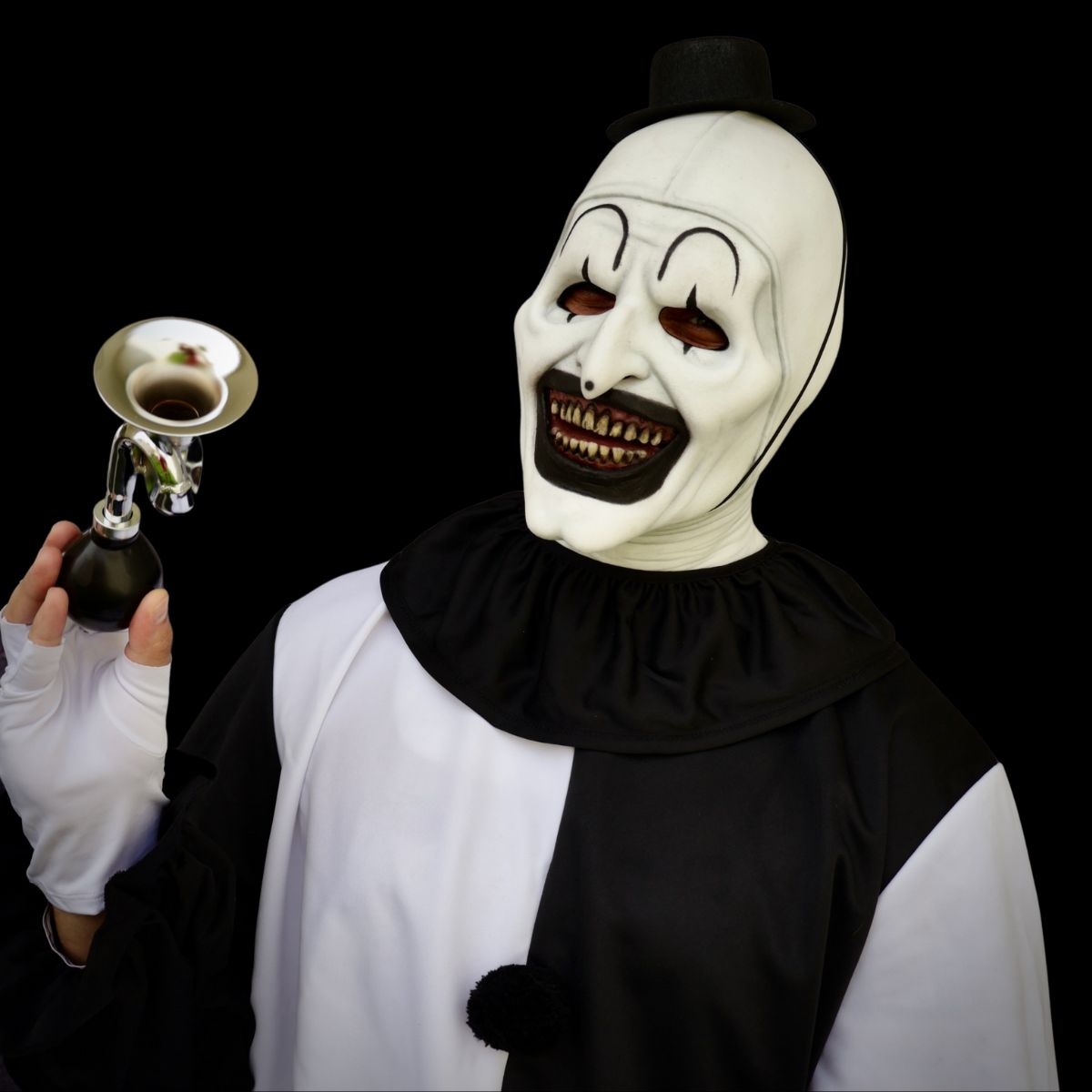 Person wearing a clown white mask with black accents and holding a bell against a black background