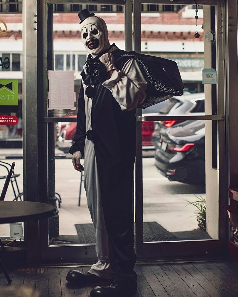 Wearing the Art the Clown mask and full costume, standing by a diner entrance with a large black bag during a Halloween night — The Terror Lab.