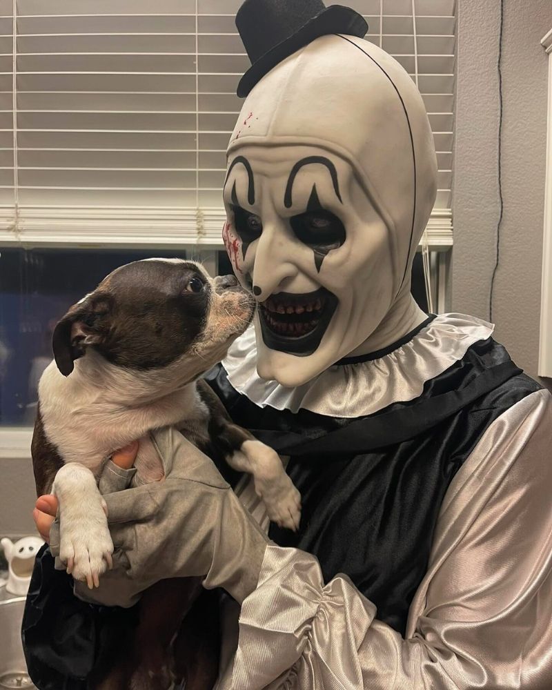 Wearing the Art the Clown mask and full costume, sharing an unexpected close moment with a small dog indoors during a Halloween night — The Terror Lab.