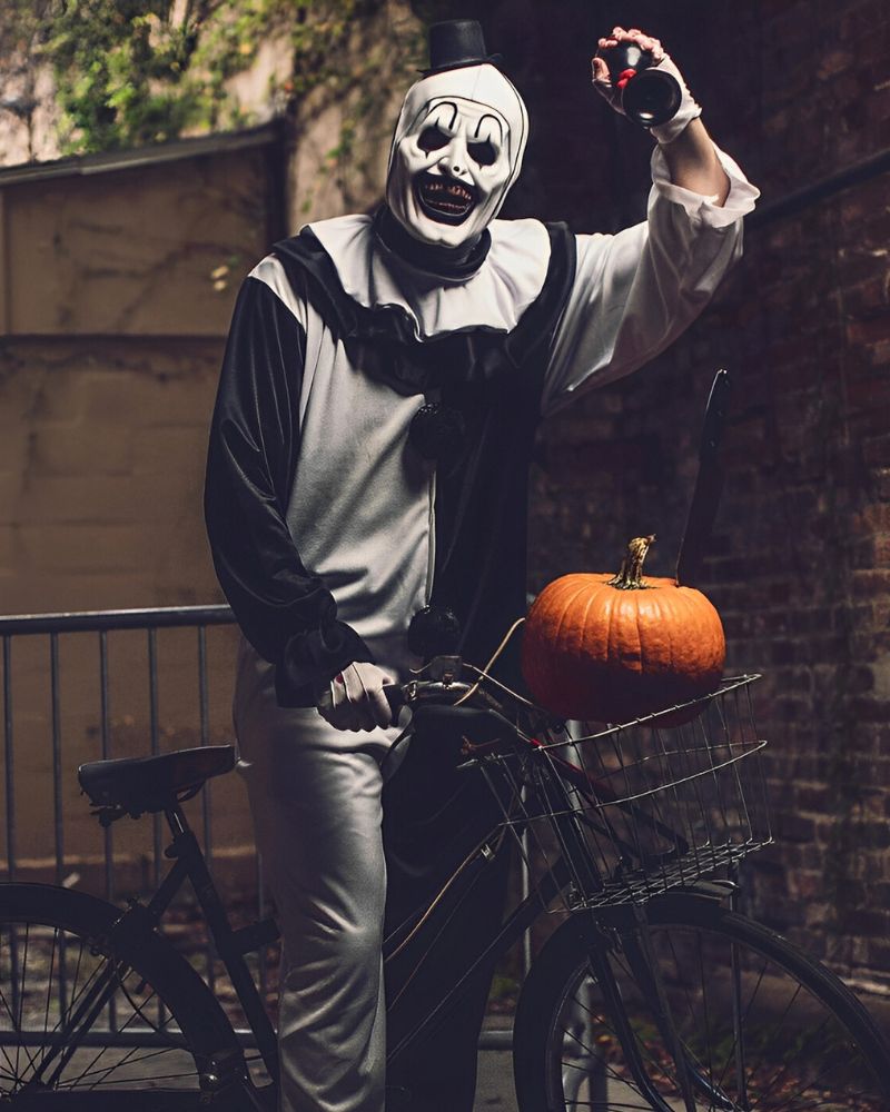Art the Clown riding a bicycle with a pumpkin and a bloody bottle, Halloween night alley scene — The Terror Lab.