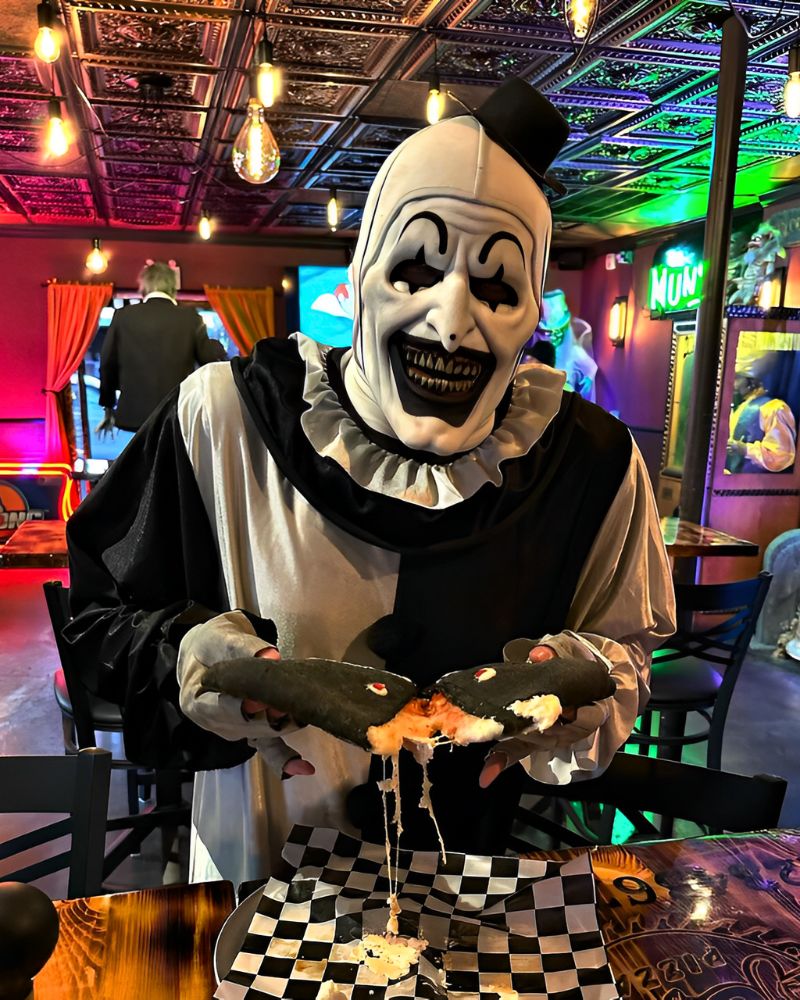 Wearing the Art the Clown mask and full costume, tearing apart a Halloween-themed stuffed sandwich in a horror-themed pizzeria — The Terror Lab.