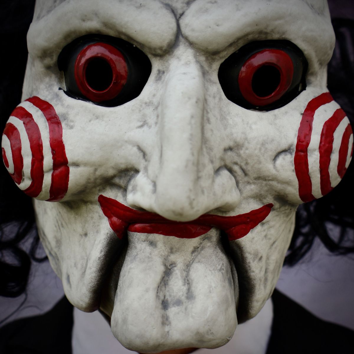 Close-up of a Billy The Puppey mask with red eyes and red and white striped sides, against a dark background.