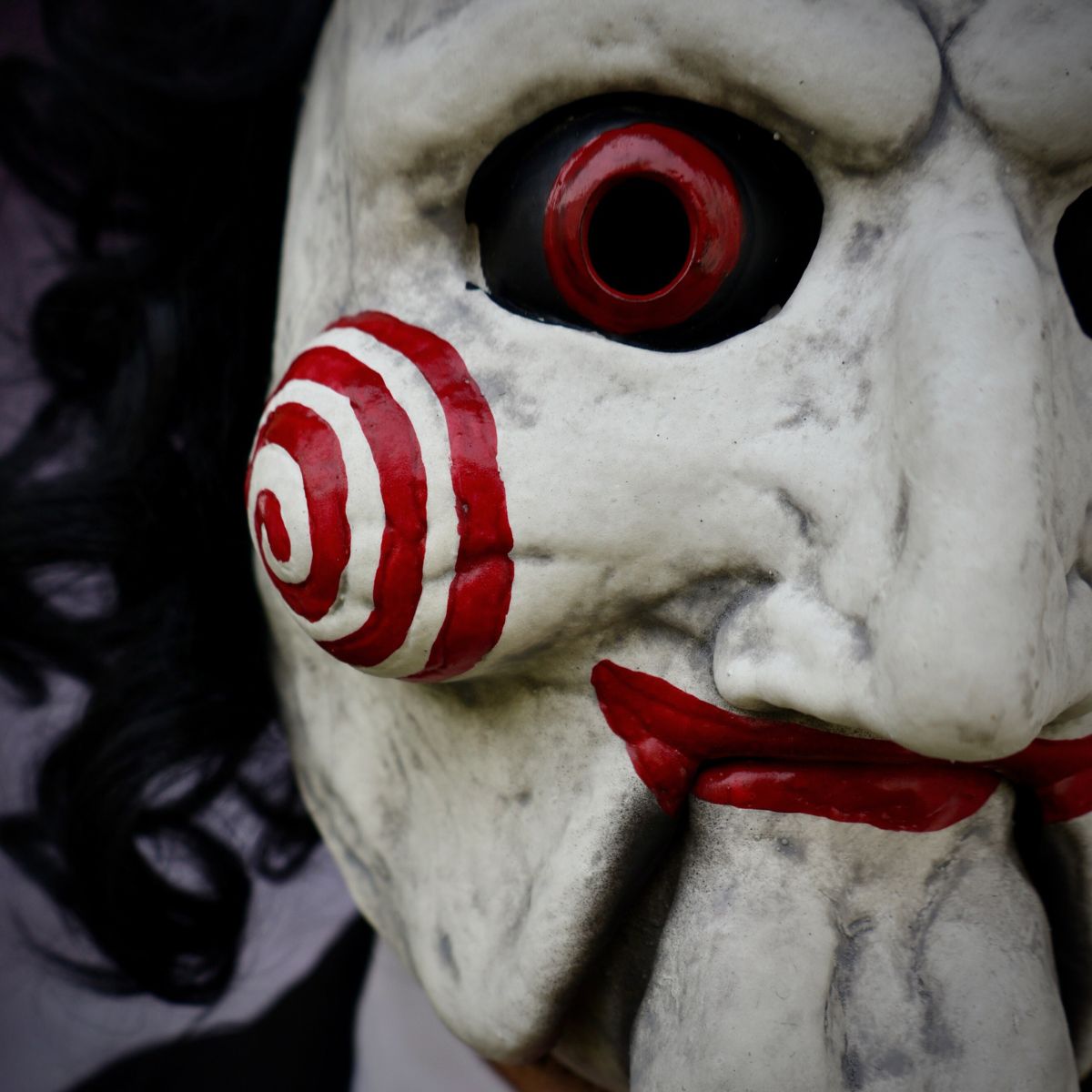 Close-up of horror billy puppet mask with red spiral design and red accents on a dark background