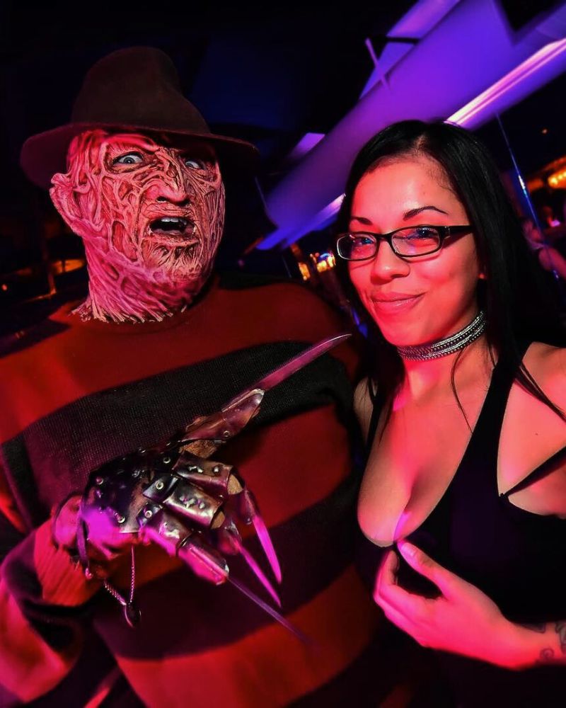 A customer in full Freddy Krueger cosplay at a packed Halloween nightclub party, wearing the mask, hat, and bladed glove from The Terror Lab.