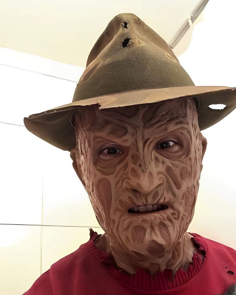 A customer wearing a full Freddy Krueger mask with hat and red sweater, captured indoors during Halloween, from The Terror Lab