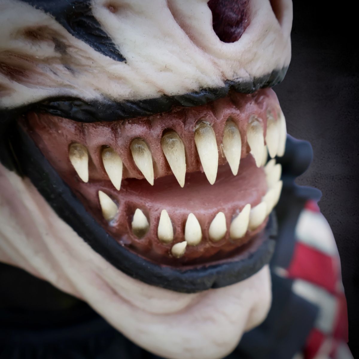 Close-up of a mask with a fierce expression and sharp teeth on a dark background of Jester The Clown