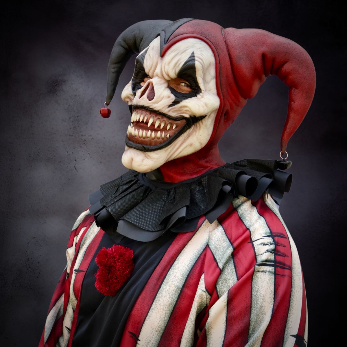 Person wearing jester dark carnival clown mask with red and black colors on a dark background