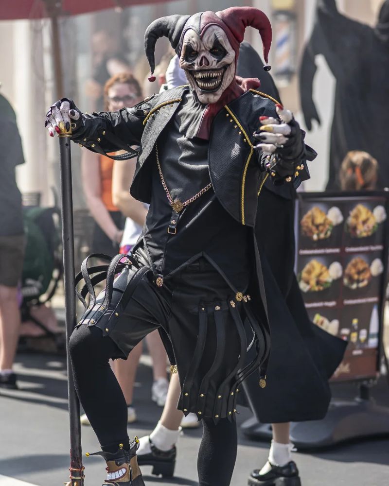 Terrifying jester mask with gold-trimmed costume, spotted in full performance mode during a Halloween street festival. The Terror Lab.