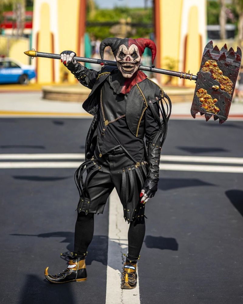 Jester mask wielding a grotesque oversized mallet, captured in broad daylight during a horror-themed park event. From The Terror Lab.