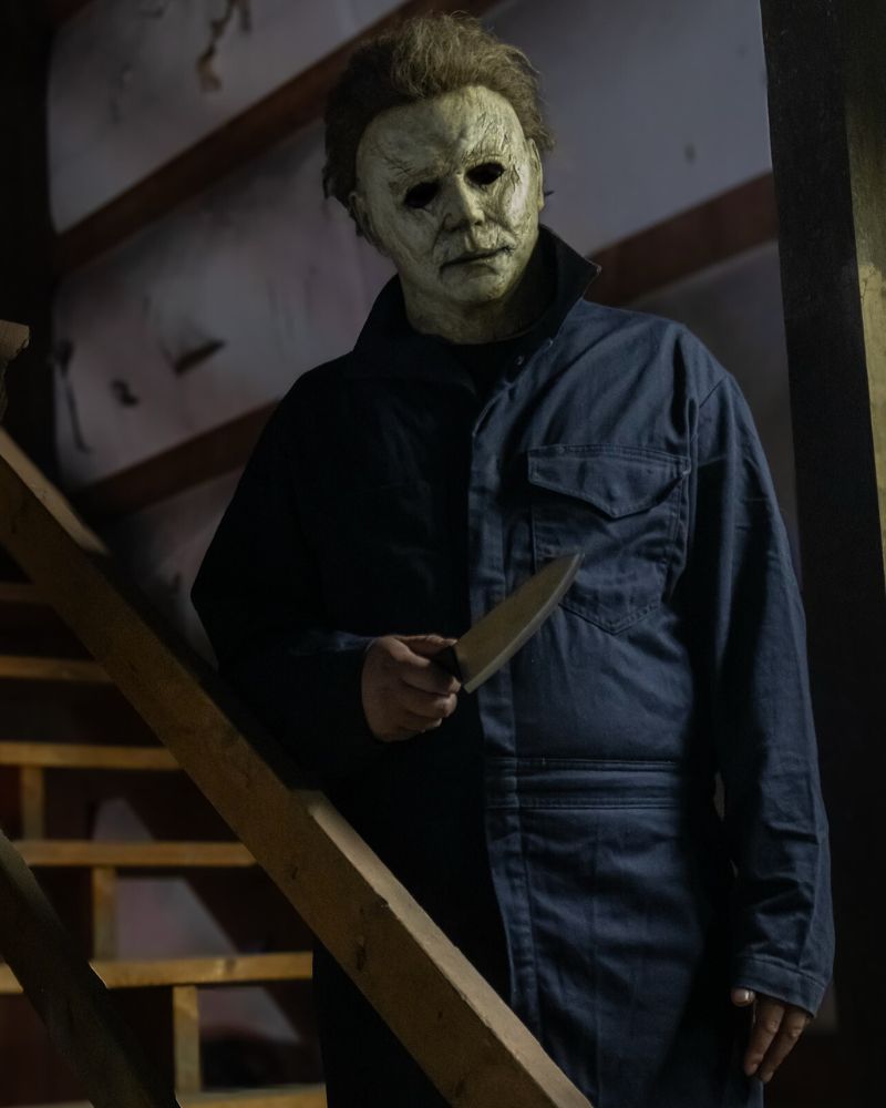 Customer in the 2018 Michael Myers mask and costume, holding a knife on a staircase inside a dimly lit house — from The Terror Lab