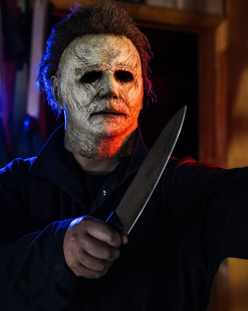 Close-up of a customer in the 2018 Michael Myers mask and costume, holding a knife with red and blue lighting — from The Terror Lab