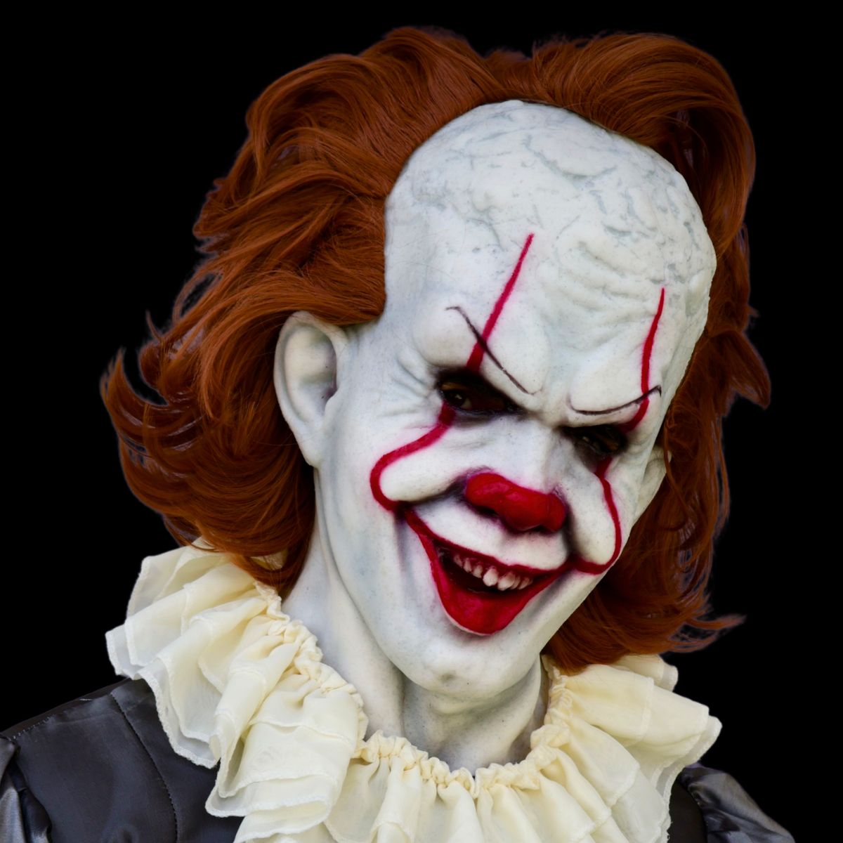 Pennywise Clown mask with red hair and white face makeup on a black background