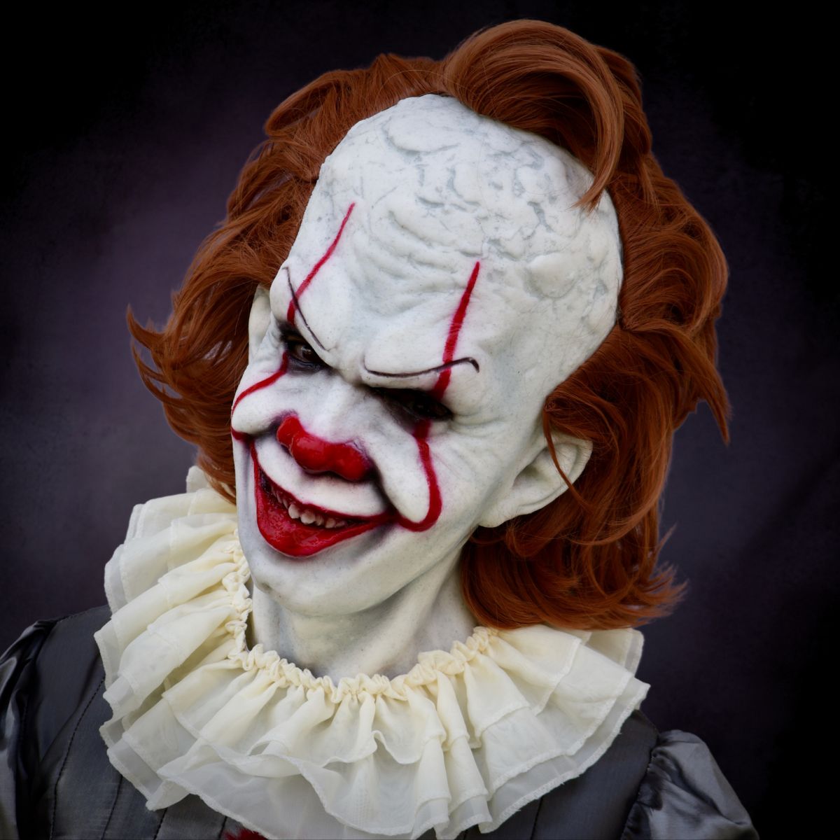 Pennywise Horror Clown mask with red hair and white ruffled collar on a dark background