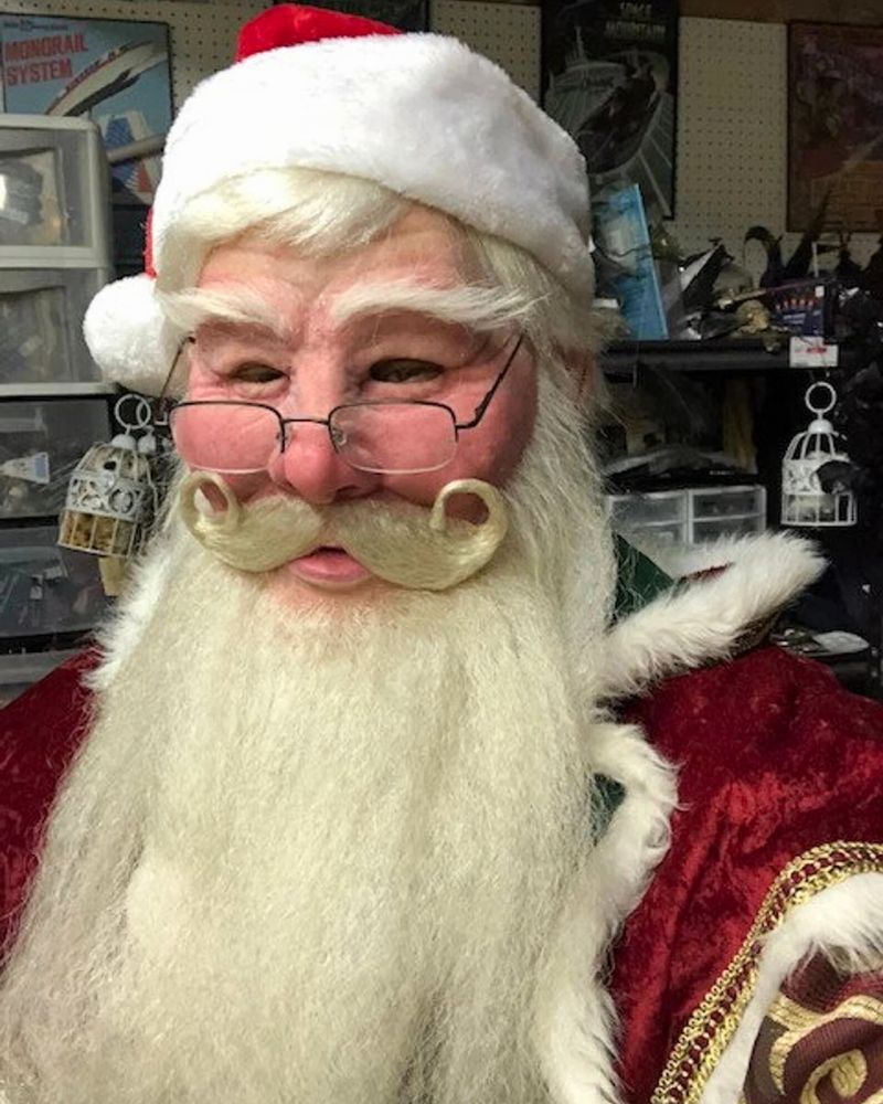 Realistic Santa Claus mask and costume worn in a workshop setting, featuring detailed eyebrows, curled mustache, and red velvet suit — The Terror Lab.