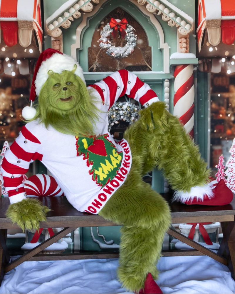 Stealer of Christmas mask and full costume with striped sweater and Santa hat, posing in a festive Christmas village set during a holiday or Halloween event — from The Terror Lab