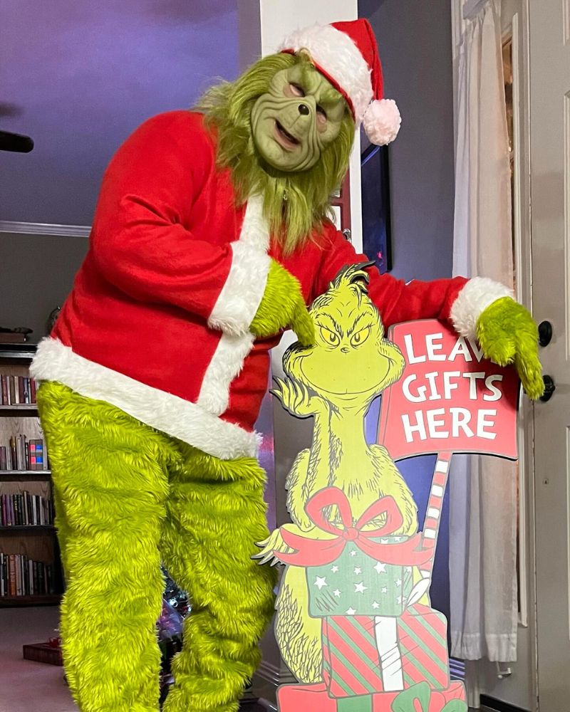Wearing the Stealer of Christmas mask and costume while posing with a cartoon cutout holding a 'Leave Gifts Here' sign during a festive home celebration — The Terror Lab.