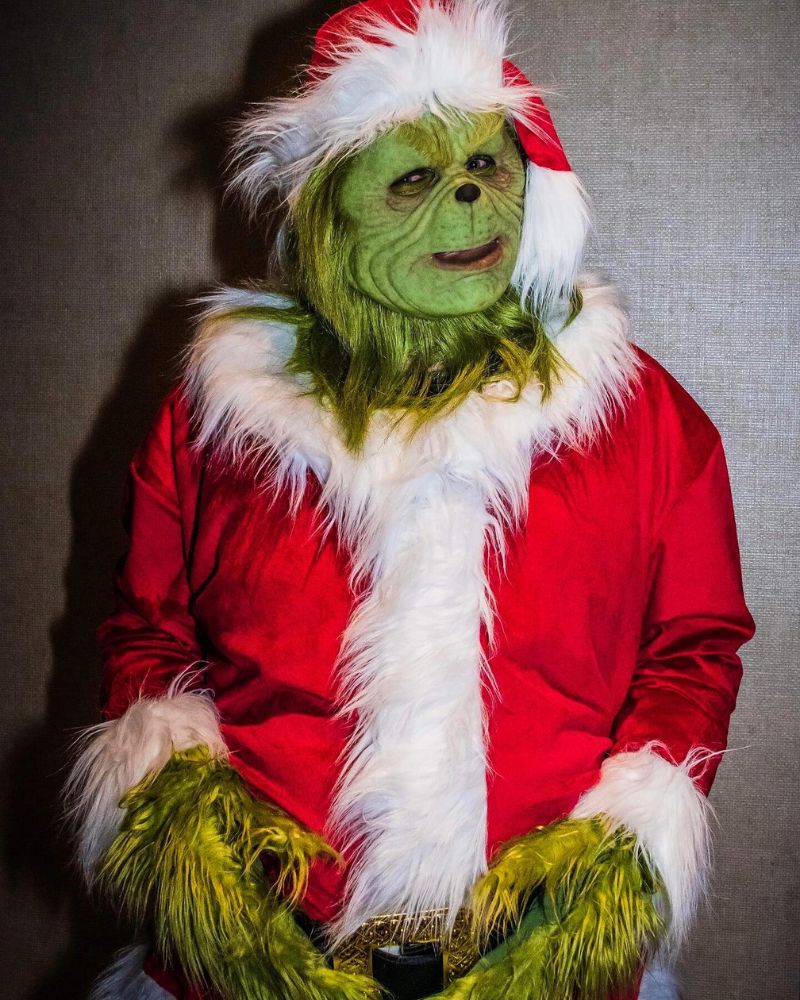 Ultra-realistic Stealer of Christmas mask and full costume captured at a holiday party indoors, showing fine green fur textures and festive red velvet suit — The Terror Lab.
