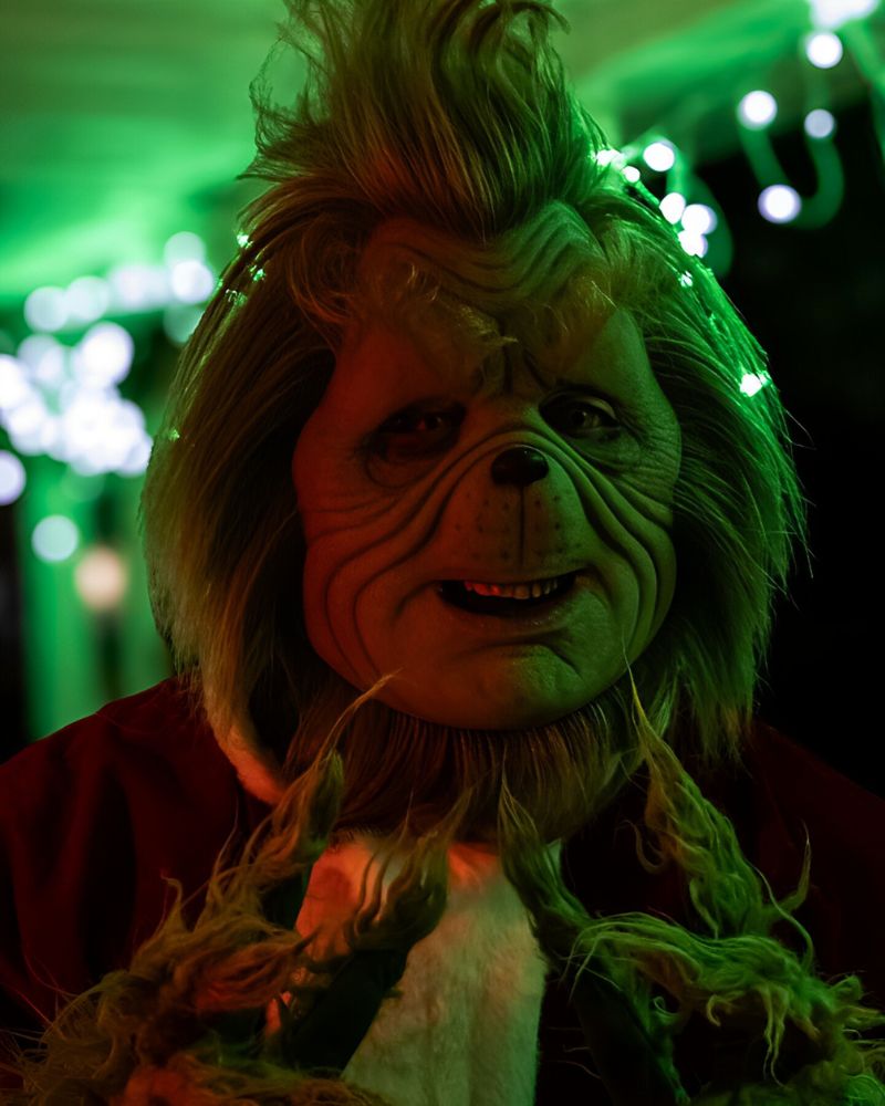 The Stealer of Christmas realistic mask glowing under green holiday lights, captured during a Halloween or Christmas night event — The Terror Lab.