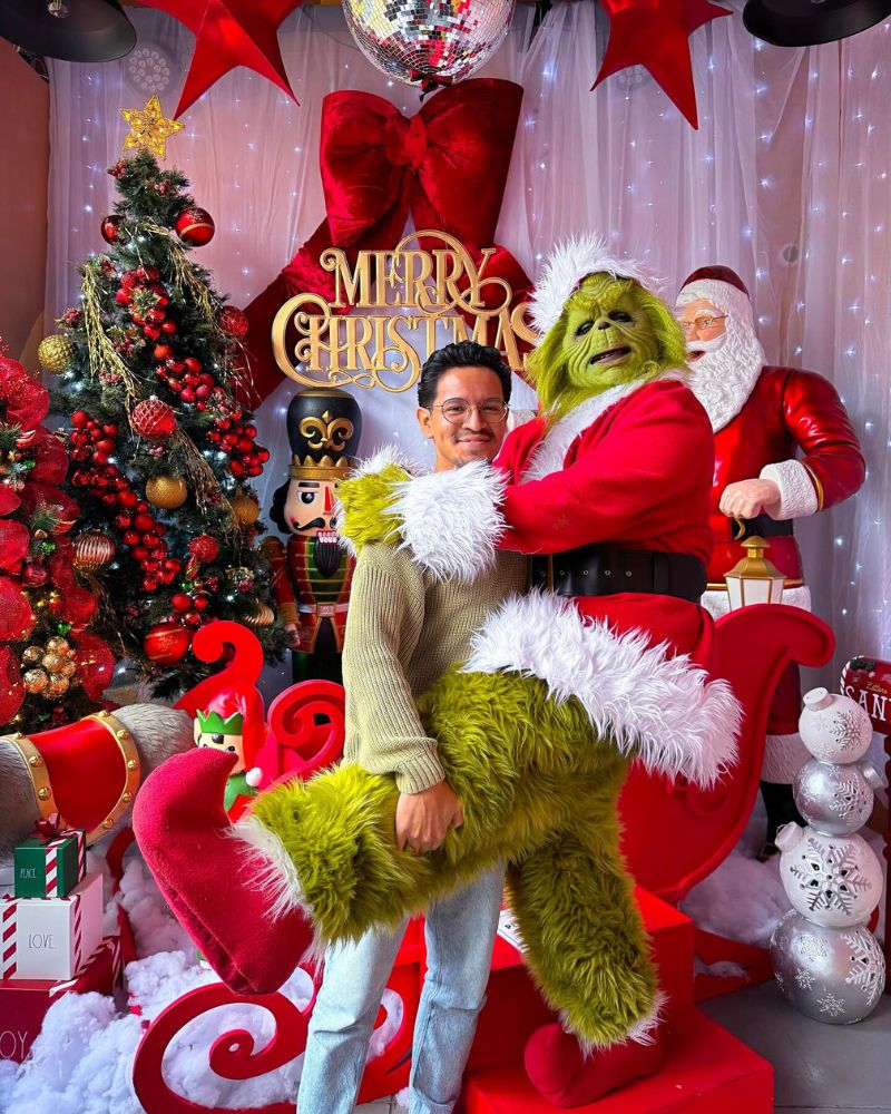 The Stealer of Christmas mask and costume spotted at a festive holiday setup, hugged by a guest in front of a Christmas tree and Santa decor — perfect for Halloween or Christmas from The Terror Lab.