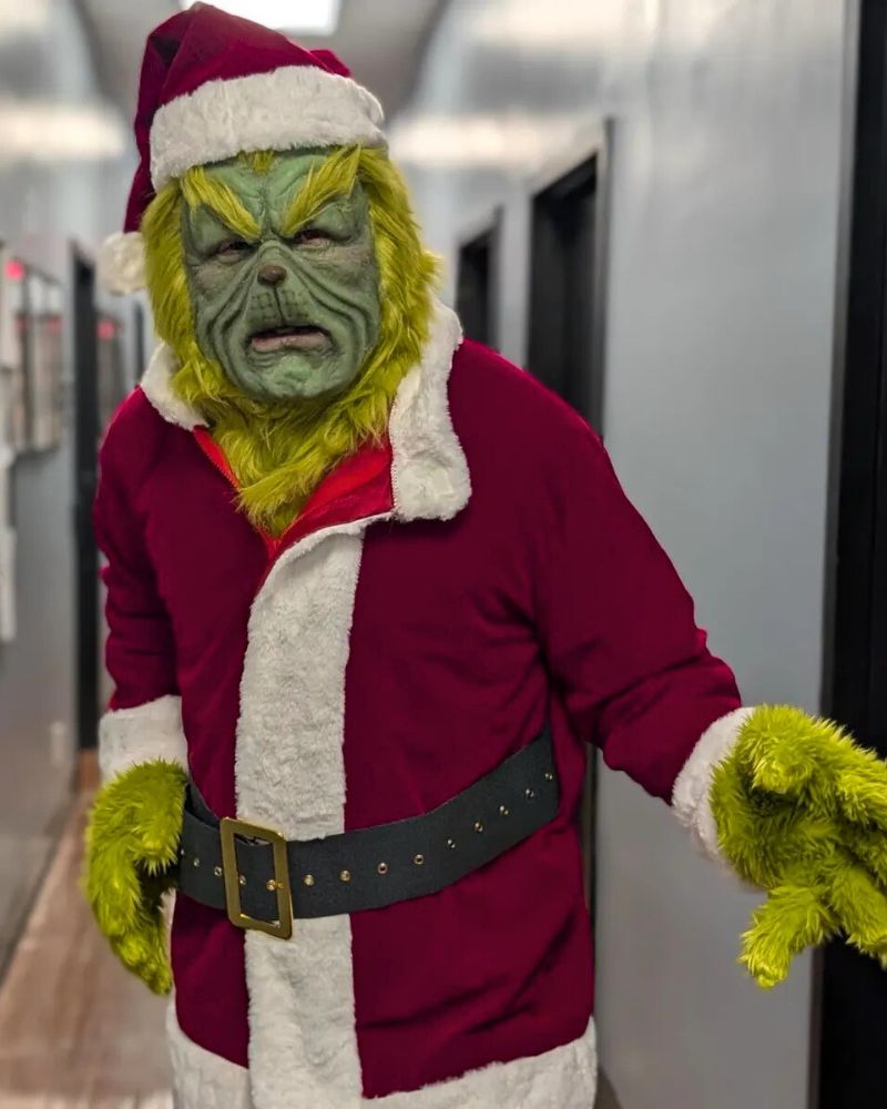 The Stealer of Christmas mask and costume worn in a hallway with Santa suit and green fur, for Halloween or Christmas events — The Terror Lab