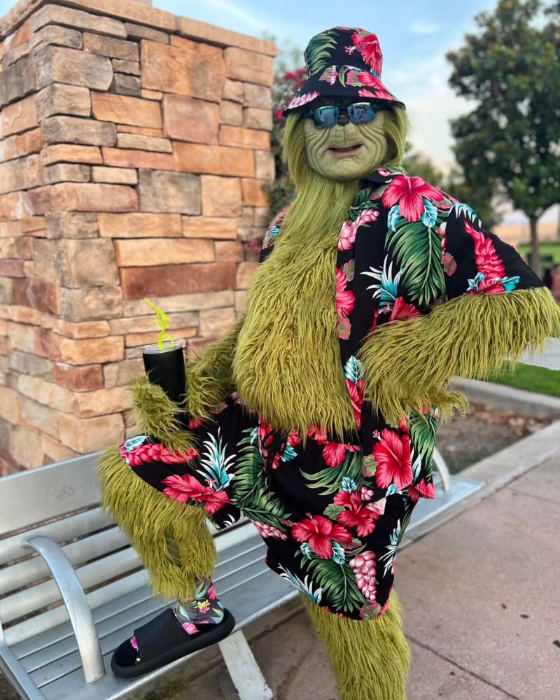The Stealer of Christmas mask and green furry costume worn with tropical vacation outfit in a sunny outdoor setting for Halloween and holiday fun — The Terror Lab
