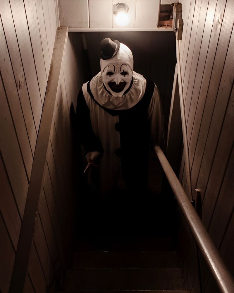 Art the Clown emerging from a dimly lit basement with a chilling grin, during a Halloween night — The Terror Lab.