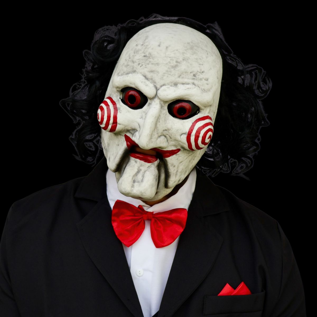 Billy the puppet mask with red eyes and red bow tie, black suit on dark background
