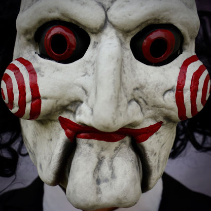 Close-up of a Billy The Puppey mask with red eyes and red and white striped sides, against a dark background.