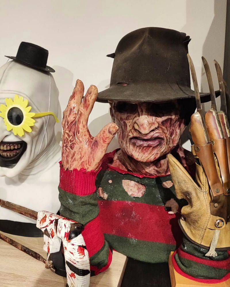 Display of Freddy Krueger and Art the Clown masks with full costume elements, claws, and bloodied props — horror collectibles setup from The Terror Lab.