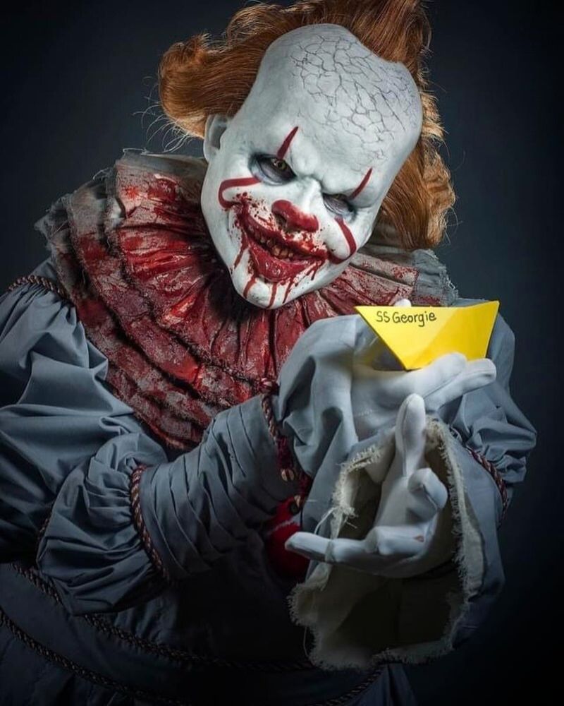 Pennywise clown mask and costume with cracked skull and blood-stained ruffles, holding Georgie’s paper boat — The Terror Lab